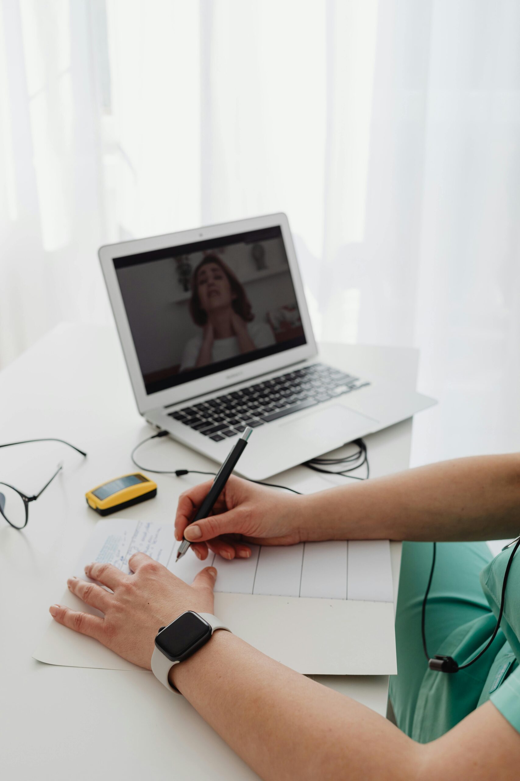 Woman taking notes during an online video call meeting with laptop in office.